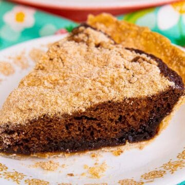 A slice of brown pie with crumb topping on a white plate with a yellow floral border.