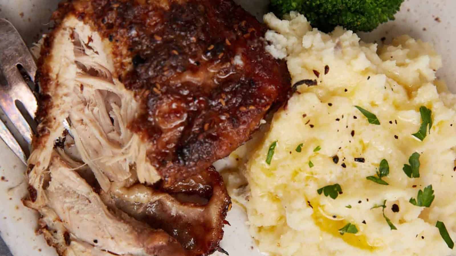 Roast chicken with mashed potatoes and broccoli on a plate, garnished with herbs and black pepper—a comforting classic inspired by slow cooker recipes.