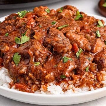 A plate of white rice topped with beef stew garnished with chopped cilantro.