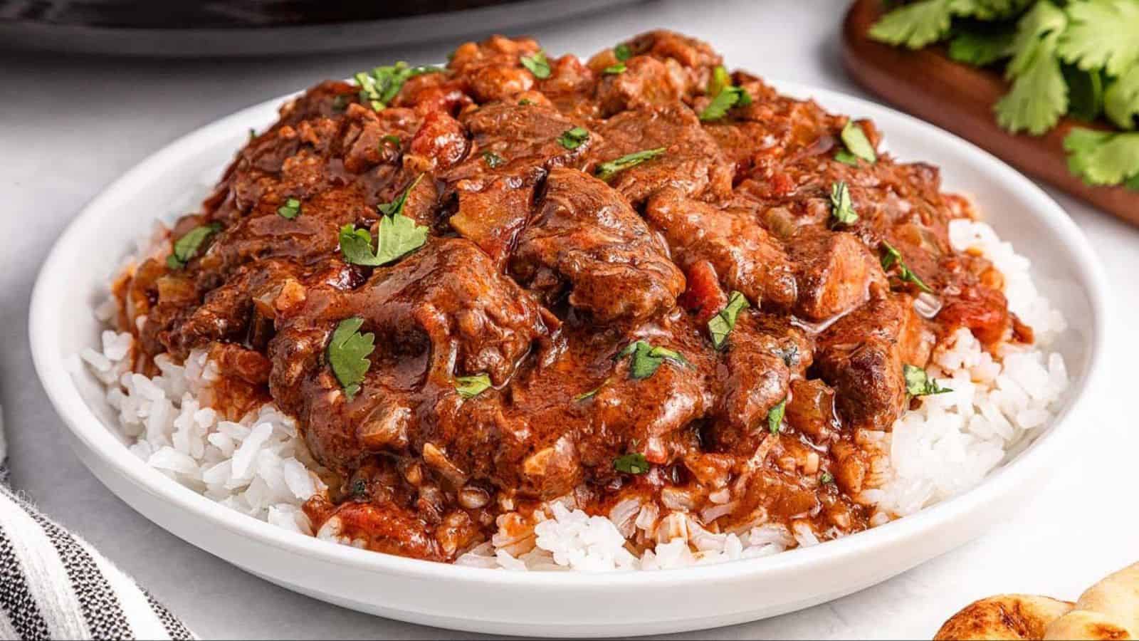 A plate of white rice topped with beef stew garnished with chopped cilantro.