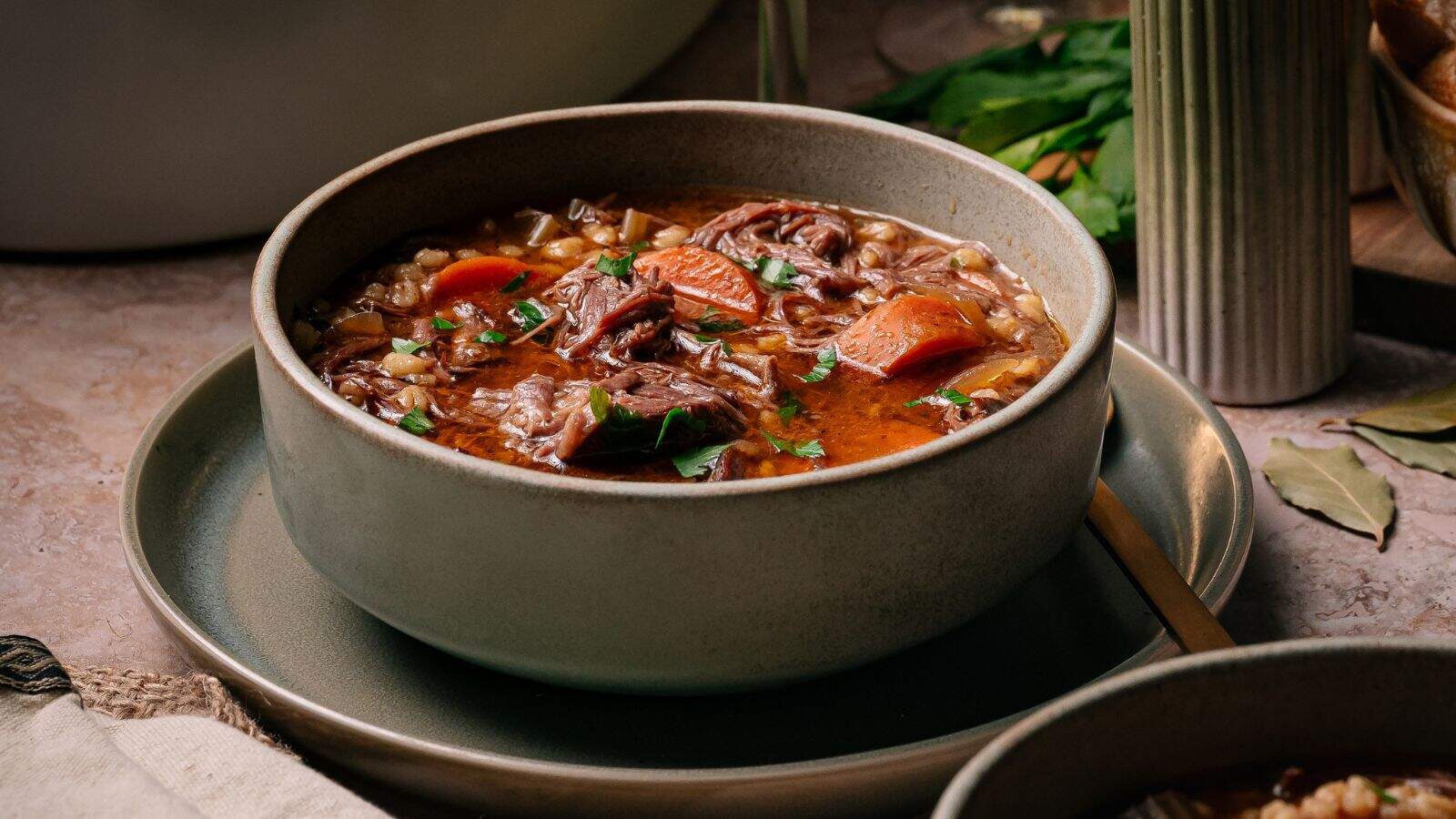 Hearty slow-cooked beef and barley soup filled with tender short rib pieces in a deep bowl.