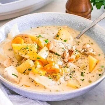 Bowl of creamy chicken stew with carrots, potatoes, herbs, and bread on the side.