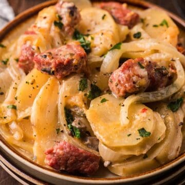 A bowl of creamy potato and sausage casserole garnished with parsley, next to a checkered napkin.