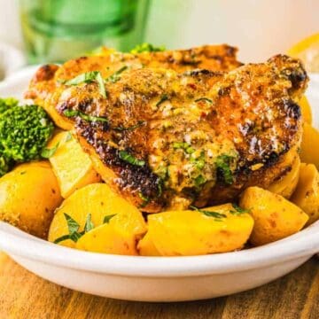 Grilled pork chops with roasted potatoes and broccoli served in a white bowl on a wooden surface.