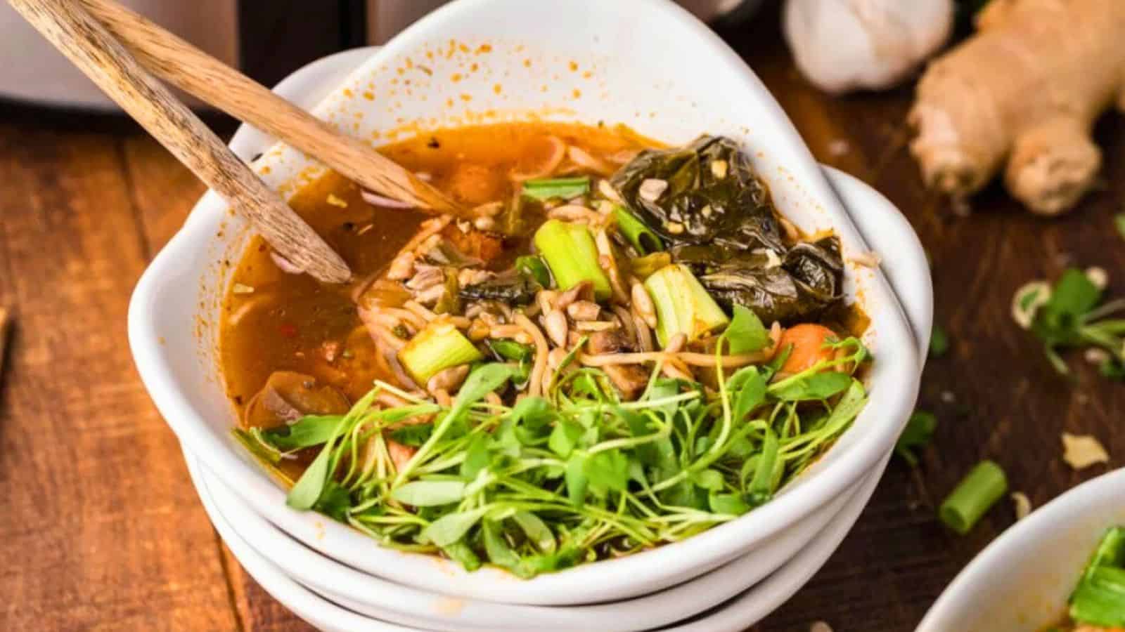 A bowl of vegetable soup topped with greens, with chopsticks resting on the bowl.