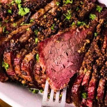 Sliced corned beef topped with herbs on a white plate, with a fork holding one slice.