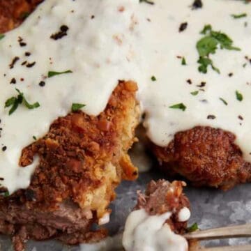 Close-up of breaded steak topped with creamy white gravy, garnished with chopped parsley and cracked black pepper.