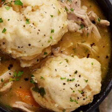 Bowl of chicken and vegetable soup topped with two large dumplings, garnished with herbs and black pepper—a comforting classic inspired by Forgotten Farmhouse Recipes.