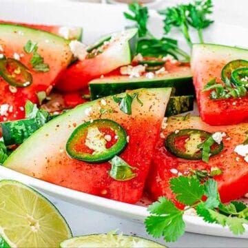 Watermelon slices topped with jalapeño, feta cheese, cilantro, and lime on a white plate.