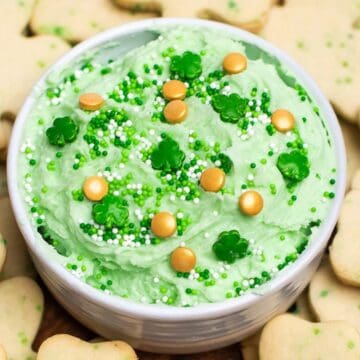 A bowl of green frosting with sprinkles, surrounded by shamrock-shaped cookies, makes a festive St. Patrick’s Day treat.