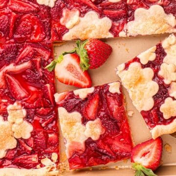 A pan of strawberry slab pie with flower-shaped crust pieces, cut into squares, with fresh strawberries on top.