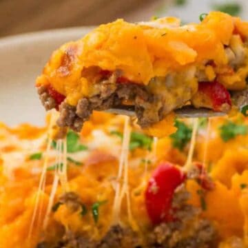 A fork lifts cheesy shepherd’s pie topped with mashed potatoes, ground beef, and red peppers.