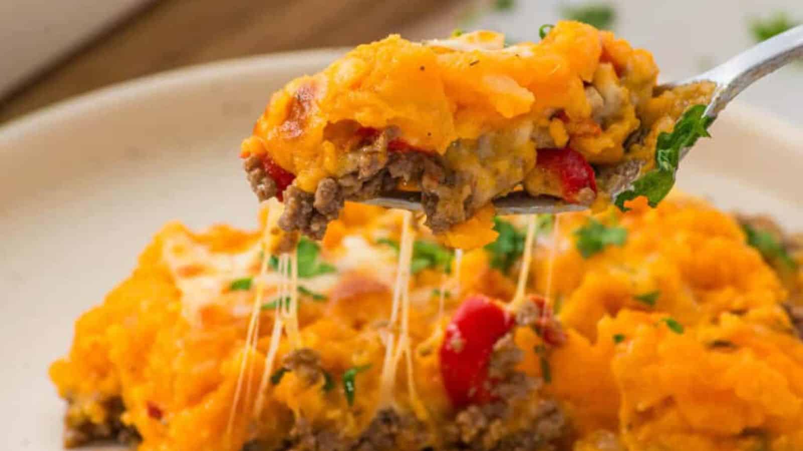 A fork lifts cheesy shepherd&rsquo;s pie topped with mashed potatoes, ground beef, and red peppers.