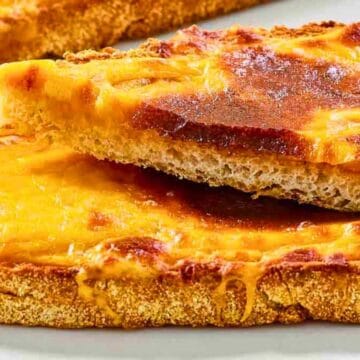 Two slices of toasted bread topped with melted, golden-brown cheddar cheese on a white plate.