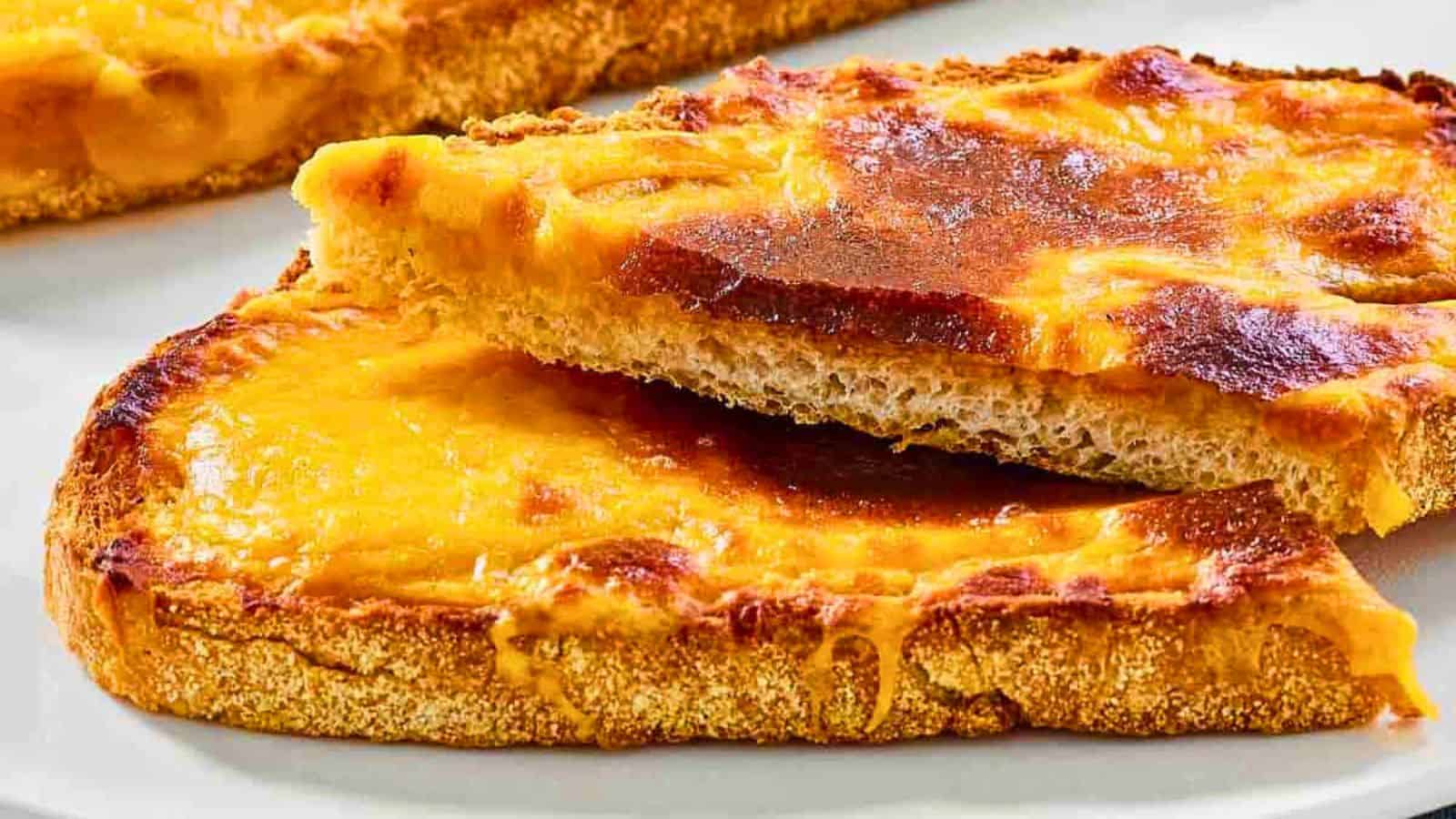 Two slices of toasted bread topped with melted, golden-brown cheddar cheese on a white plate.