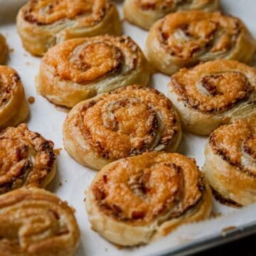 Golden cheese and pastry pinwheels, reminiscent of vintage appetizers, arranged on a parchment-lined baking tray.