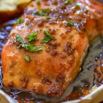 Glazed salmon fillet garnished with herbs, resting in a pan with a rich, dark sauce—an elegant alternative to traditional meat-free dinners.