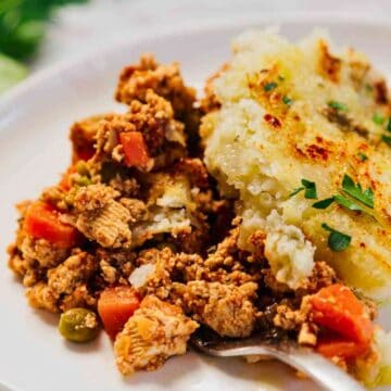 A plate of shepherd's pie with ground meat, vegetables, and mashed potato topping, garnished with herbs.
