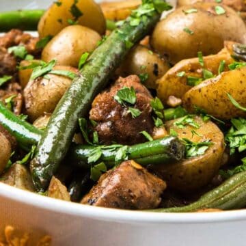 Close-up of a bowl filled with green beans, potatoes, meat chunks, and herbs.