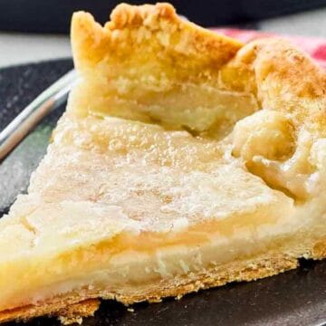 A slice of creamy custard pie on a black plate with a fork, set on a red plaid napkin.