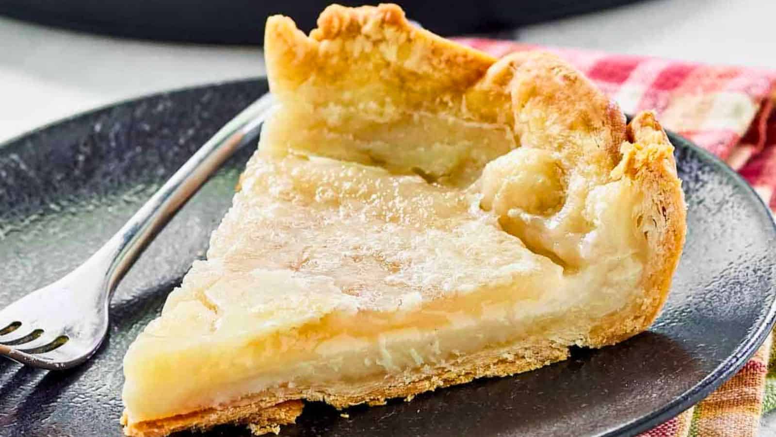 A slice of creamy custard pie on a black plate with a fork, set on a red plaid napkin.
