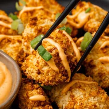 Crispy breaded cauliflower bites with orange sauce, garnished with green onions, and chopsticks picking one up-a delicious plant-based twist inspired by classic chicken recipes.