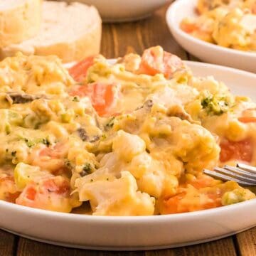 A plate of cheesy vegetable casserole, perfect as one of your favorite vegetable sides, with a fork and slices of bread in the background.