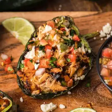 Stuffed poblano peppers with chicken and pico de gallo, served with a bowl of salsa and lime wedges.