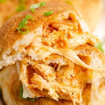 Close-up of a stuffed bread roll filled with shredded chicken and melted cheese, garnished with chopped green onions.