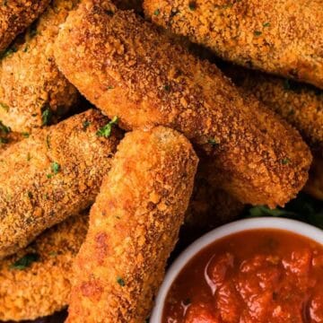 A pile of crispy breaded mozzarella sticks with a bowl of marinara sauce for dipping.