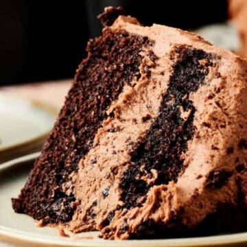 A slice of rich chocolate cake with chocolate frosting on a plate.