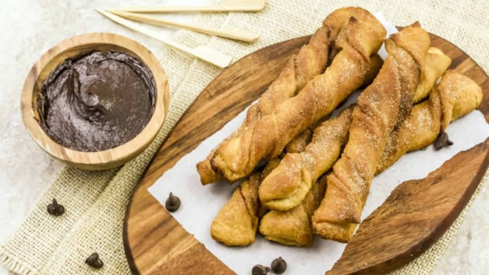Air Fryer Churros on a wooden board with chocolate sauce in a bowl in the background.