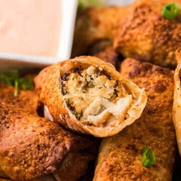 Close-up of crispy egg rolls with a creamy dipping sauce, garnished with sliced green onions.