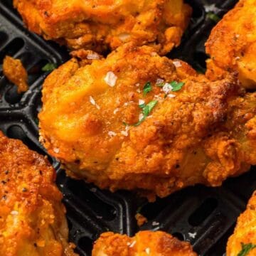 Close-up of crispy fried chicken pieces with golden breading, sprinkled with herbs and coarse salt.