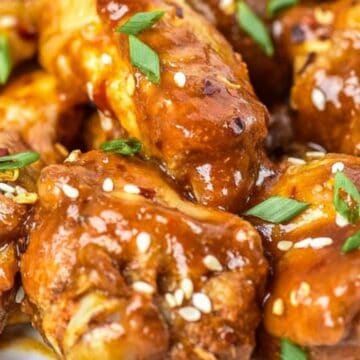 Close-up of saucy chicken wings topped with sesame seeds and chopped green onions.