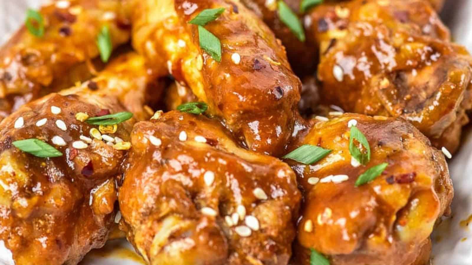 Close-up of glazed chicken wings garnished with sesame seeds and chopped green onions on a white plate.