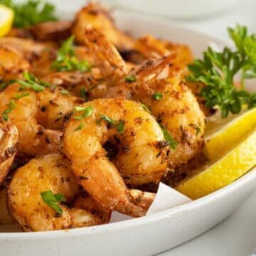 A plate of seasoned grilled shrimp garnished with parsley and lemon slices.