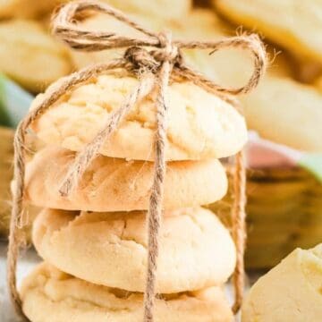 A stack of cookies tied with twine, with more cookies and a colorful cloth in the background.