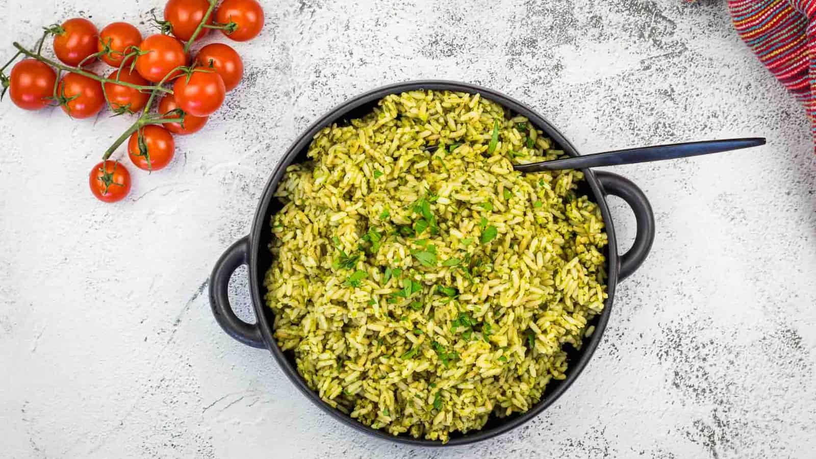 Arroz Verde rice in a black pan with tomatoes and herbs.