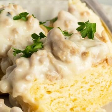 Biscuits topped with creamy sausage gravy, a nod to vintage recipes, and garnished with parsley on a white plate with a fork.