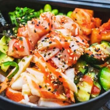 A colorful poke bowl with diced fish, avocado, cucumber, greens, and sesame seeds, drizzled with sauce—a delicious option for high-protein dinners.