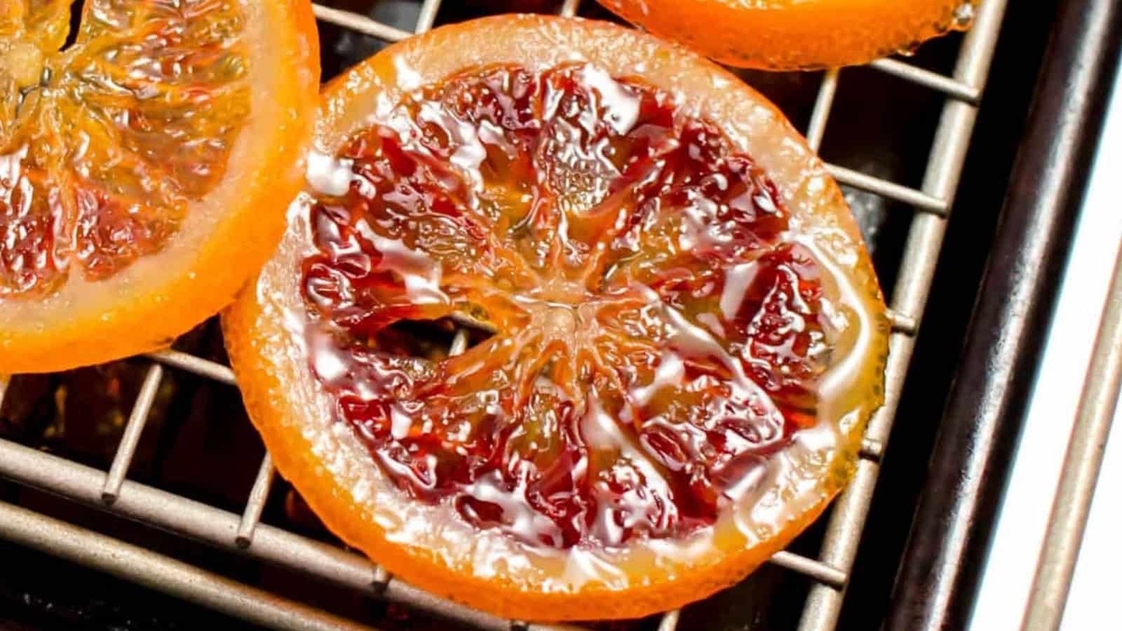 A close-up of a glossy, candied orange slice resting on a metal cooling rack.