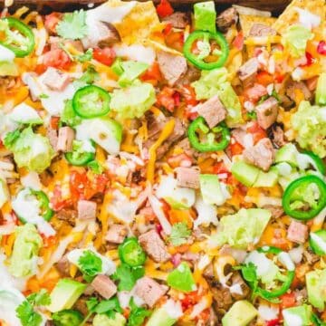 Sheet pan nachos topped with melted cheese, steak, jalapeños, guacamole, pico de gallo, cilantro, and sour cream—perfect for your next fiesta or as a crowd-pleasing addition to Cinco de Mayo recipes.