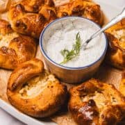 Golden pastries filled with cheese, served with a creamy herb dip in a bowl, garnished with fresh dill.