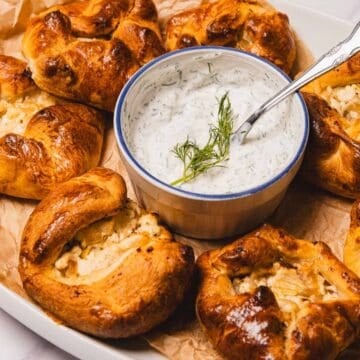 Golden pastries filled with cheese, served with a creamy herb dip in a bowl, garnished with fresh dill.