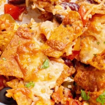 A close-up of a cheesy nacho casserole with tortilla chips, melted cheese, beans, and vegetables.