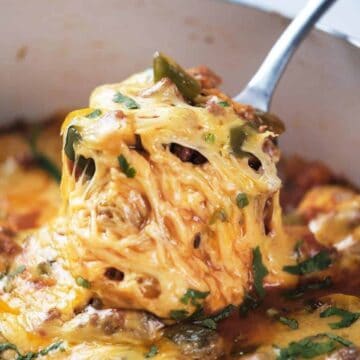 A serving spoon lifts cheesy, baked spaghetti from a casserole dish, topped with melted cheese and herbs—a perfect choice for budget dinners.