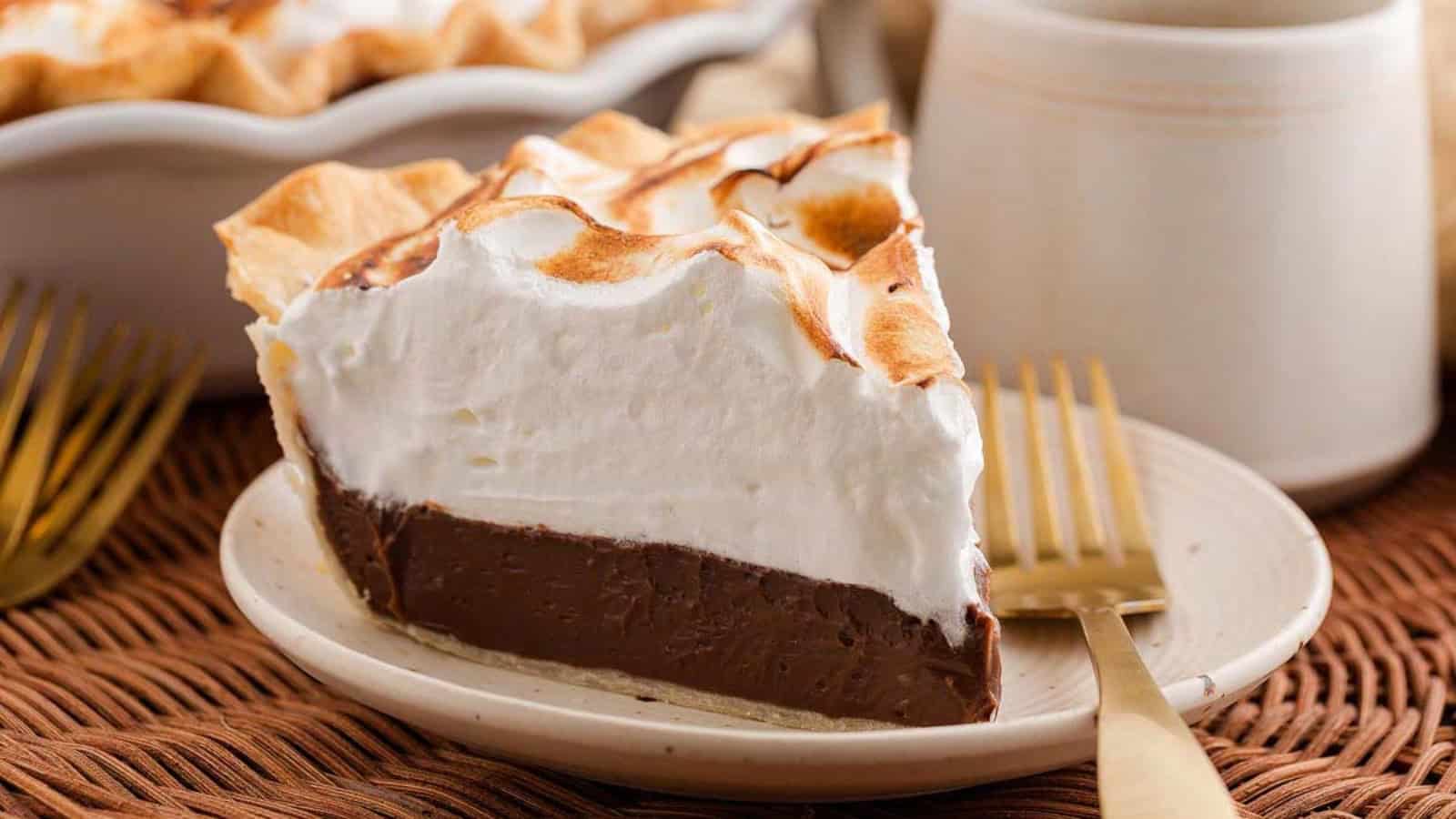 A slice of chocolate pie with fluffy whipped topping on a plate with a gold fork.