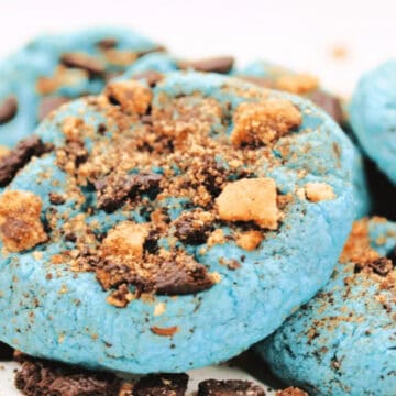 Blue cookies topped with crumbled chocolate and cookie pieces, arranged on a white surface.