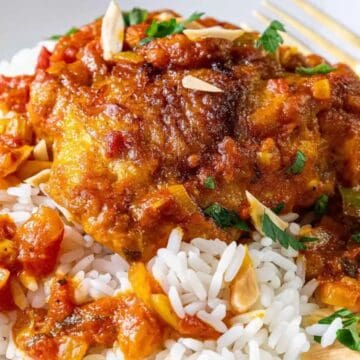 Chicken in tomato sauce with vegetables served over white rice, garnished with herbs and sliced almonds.